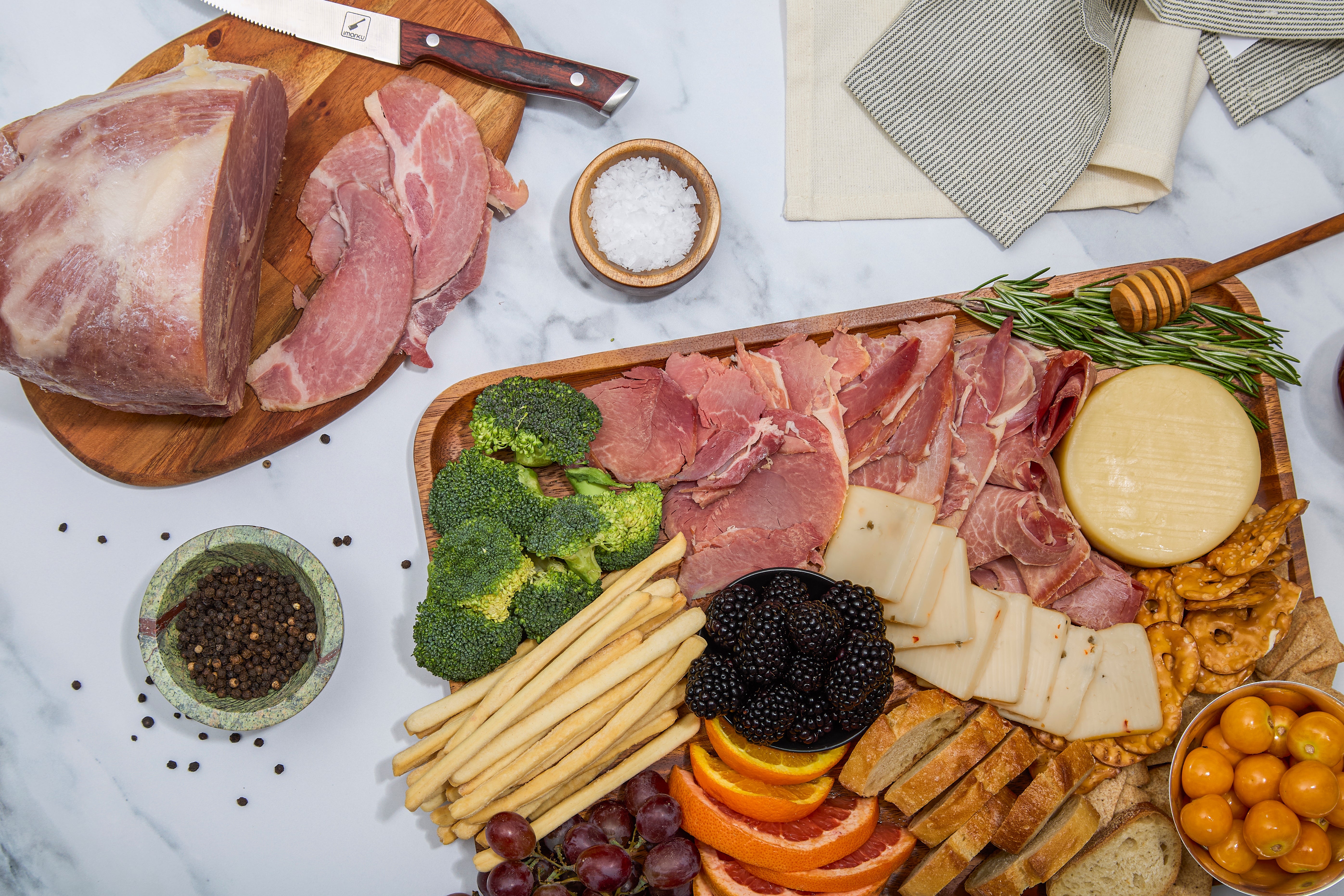 Slices of Turner Ham, cheeses, bread and vegetables on a wooden board with a marble background