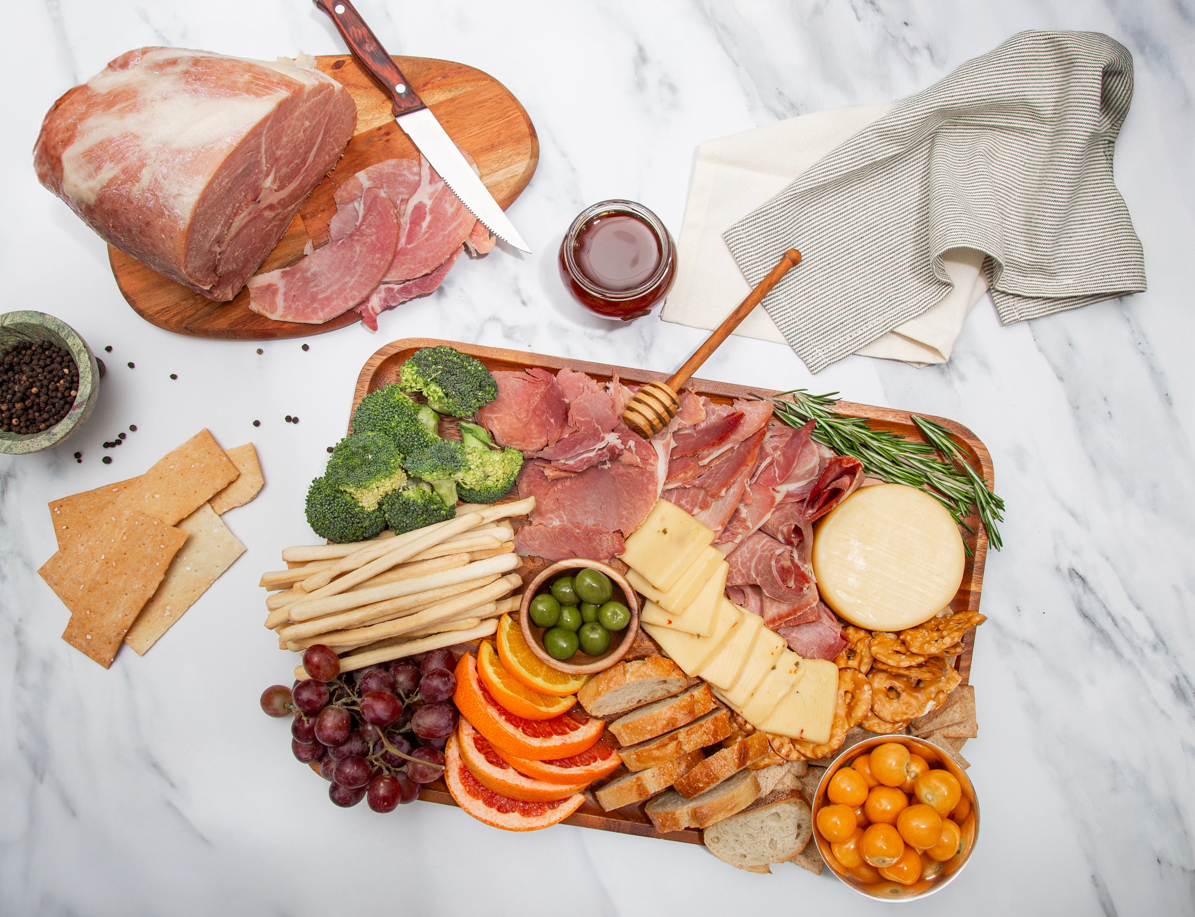 Assorted cured Turner Ham slices, cheeses, fruits, and crackers on a wooden board with a marble background.