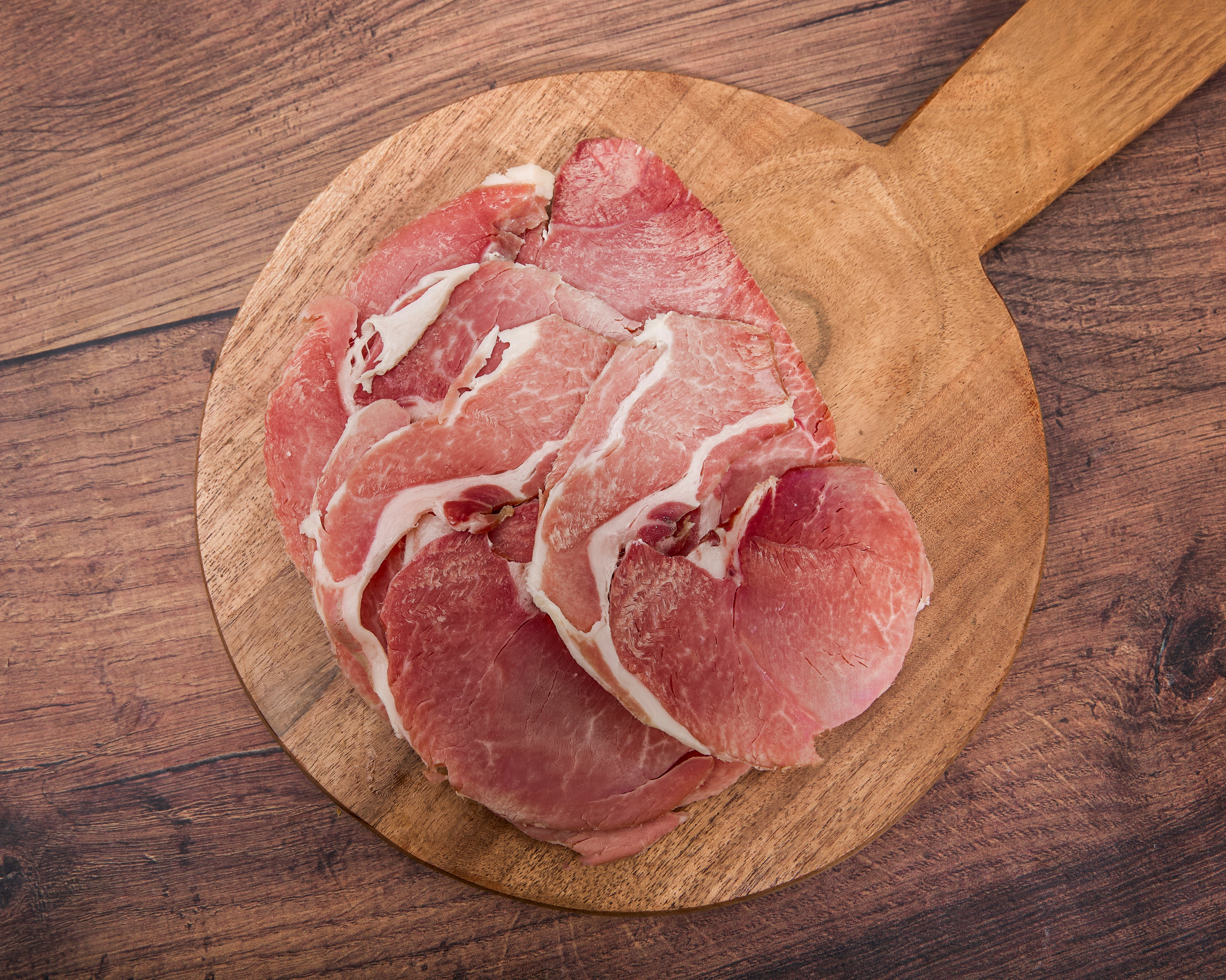 Cooked slices of Turner Ham on a round wooden cutting board