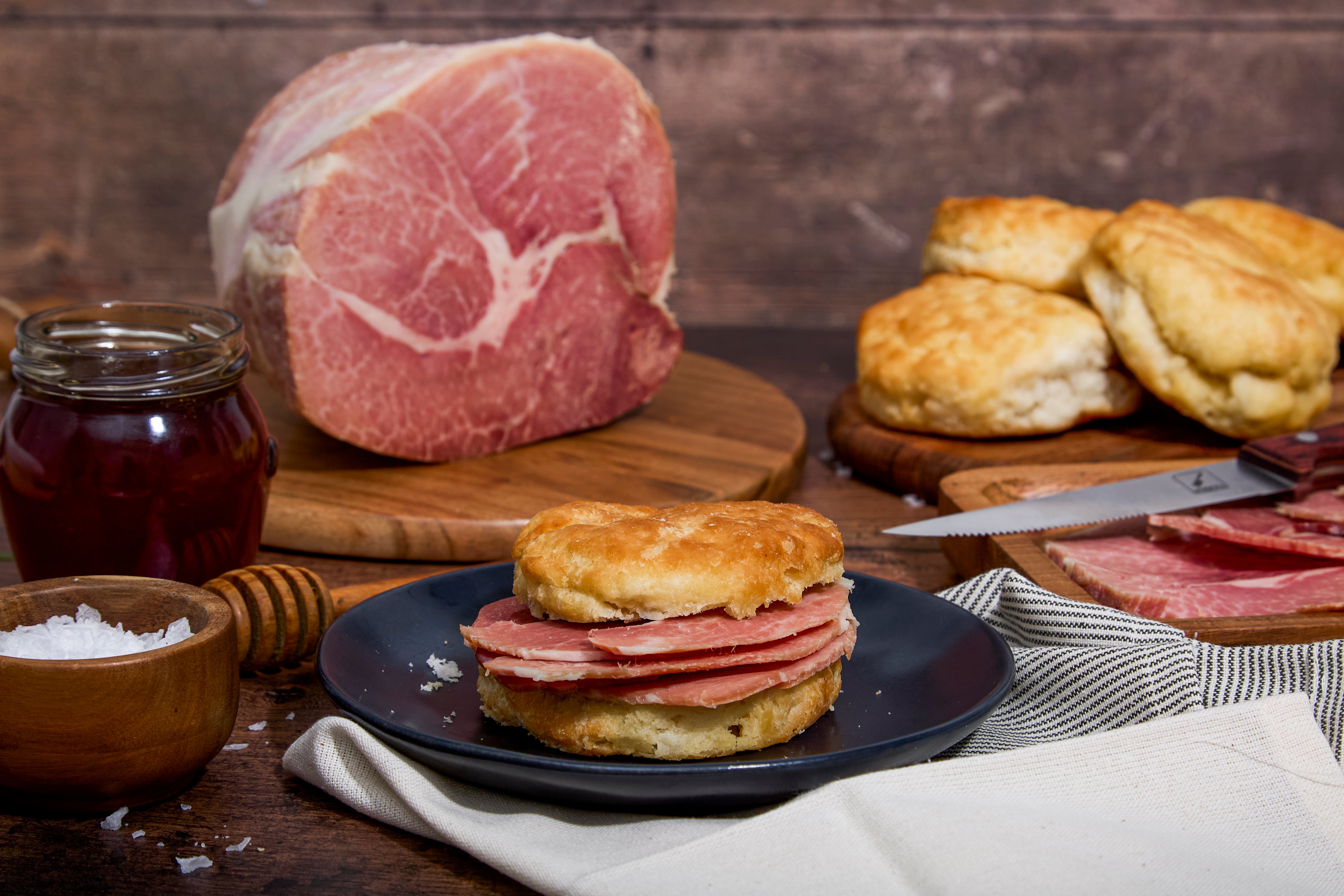 Biscuit sandwich with Turner Ham slices on a plate, with cured Turner Hams and biscuits in the background.