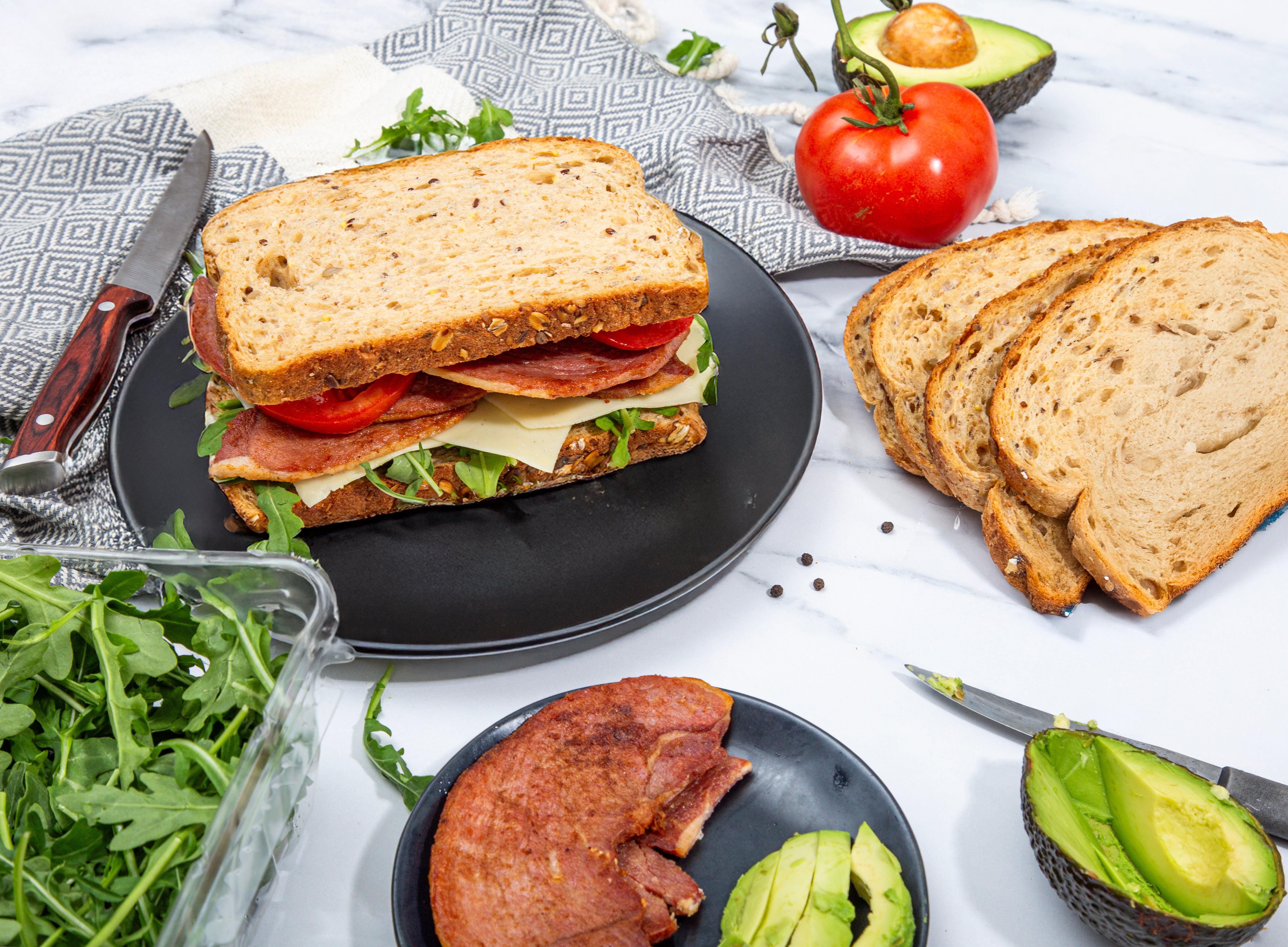 Lunch setup with a sandwich, Turner Ham slices, and fresh ingredients on a white surface.