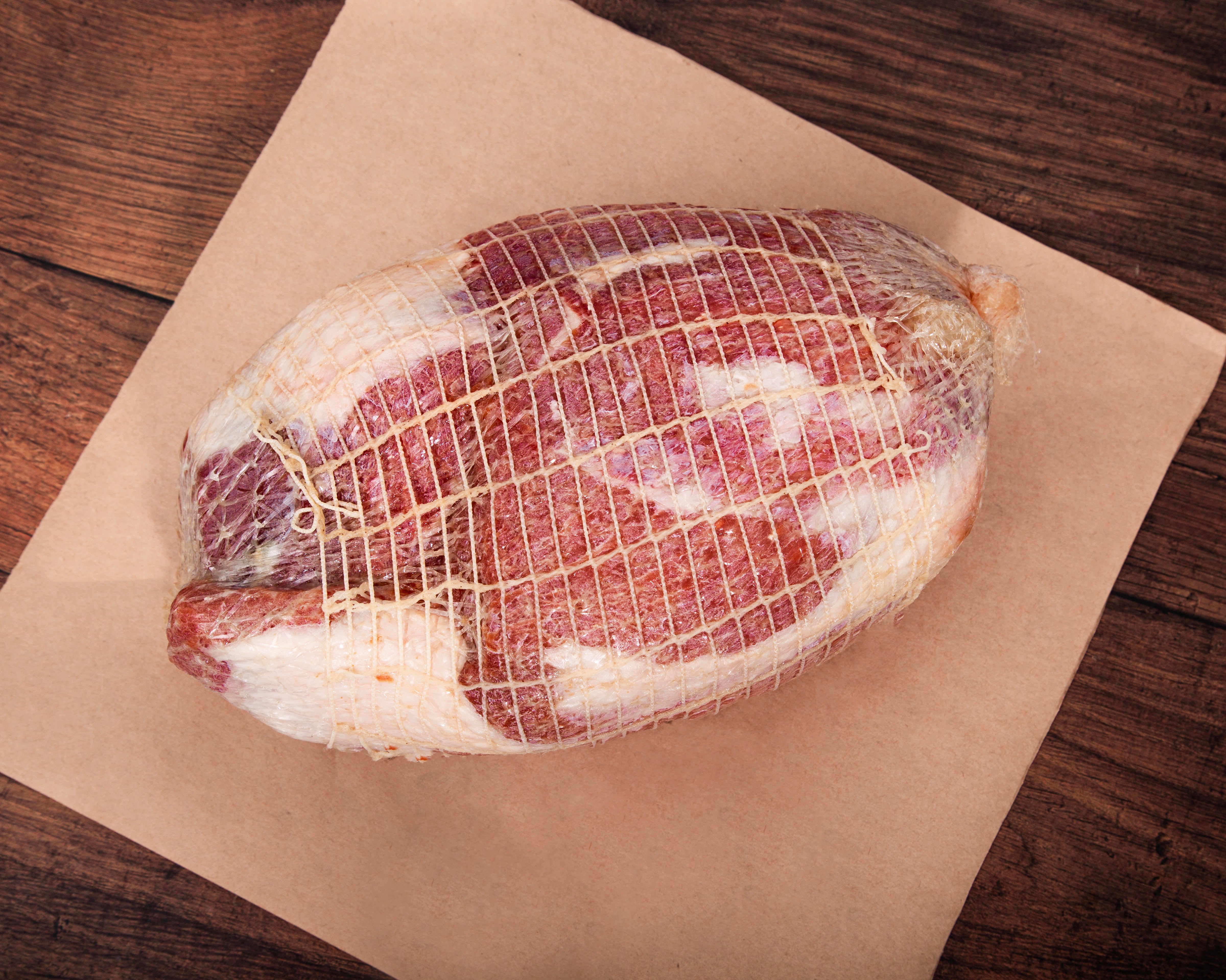Uncooked whole Turner Ham in netting on brown paper with a wooden background