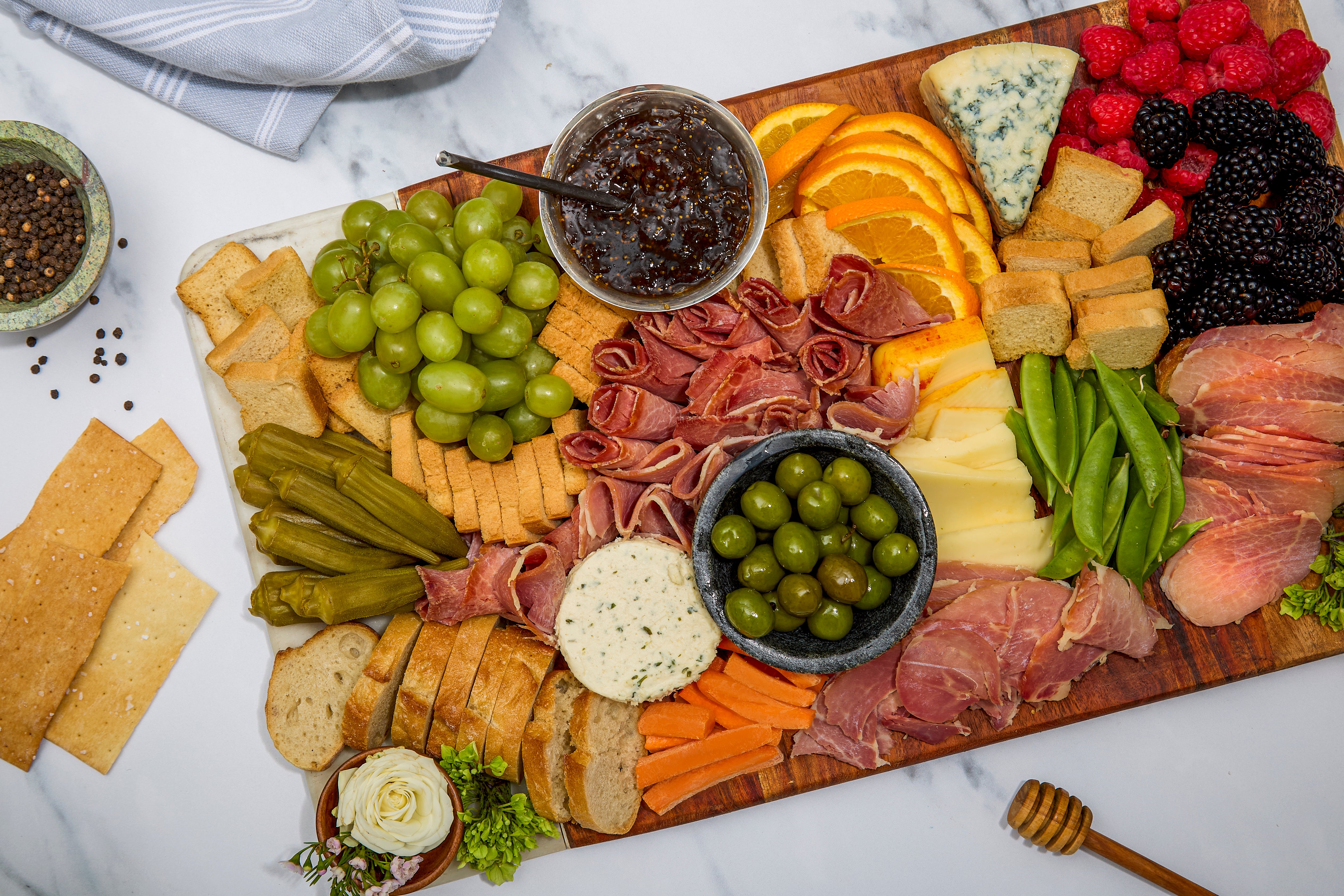 Assorted charcuterie board with slices of Turner Ham, cheeses, fruits, and vegetables on a wooden board.