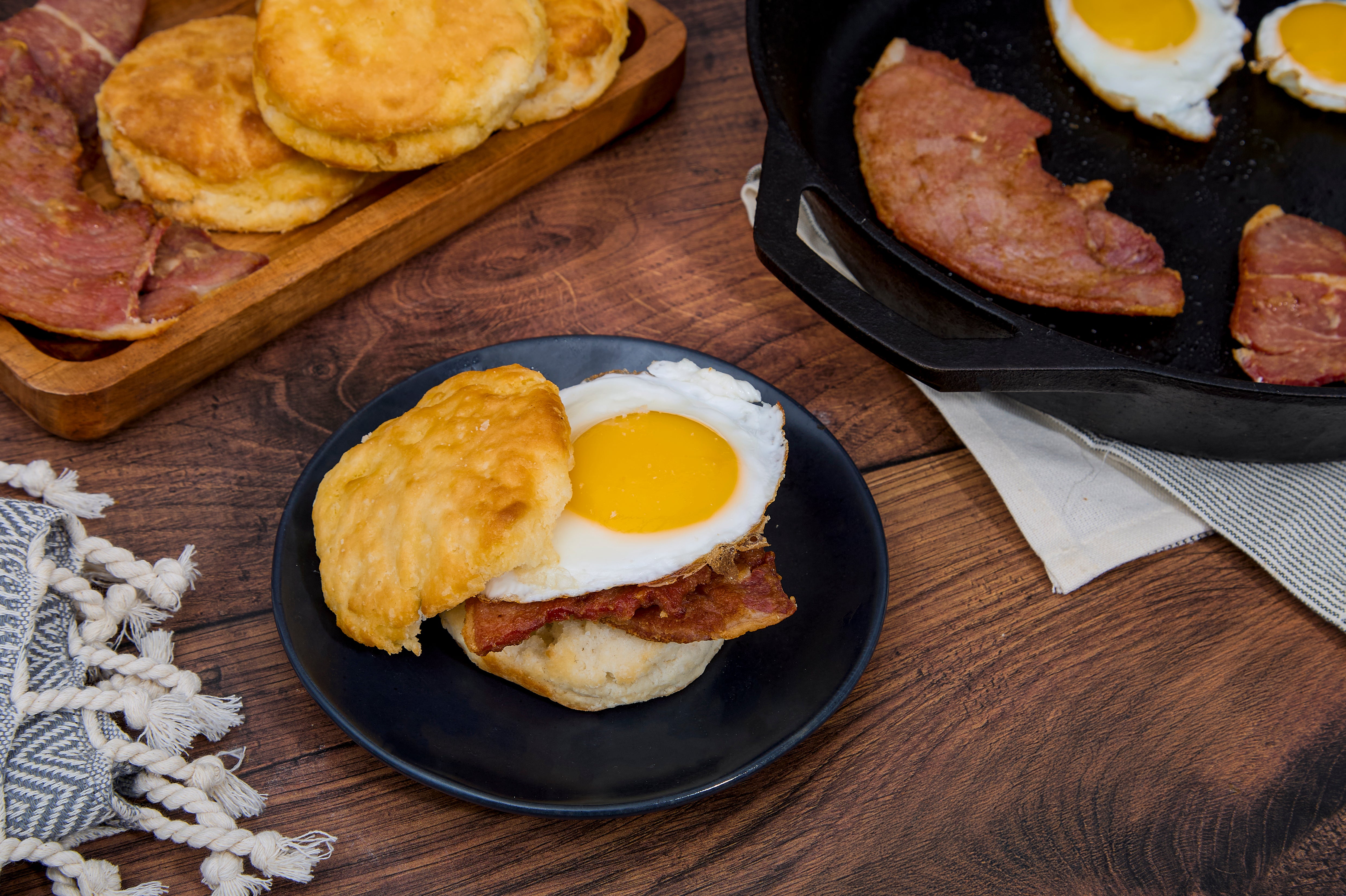 A biscuit with Turner Ham slices and a fried egg on a plate surrounded by a breakfast setting